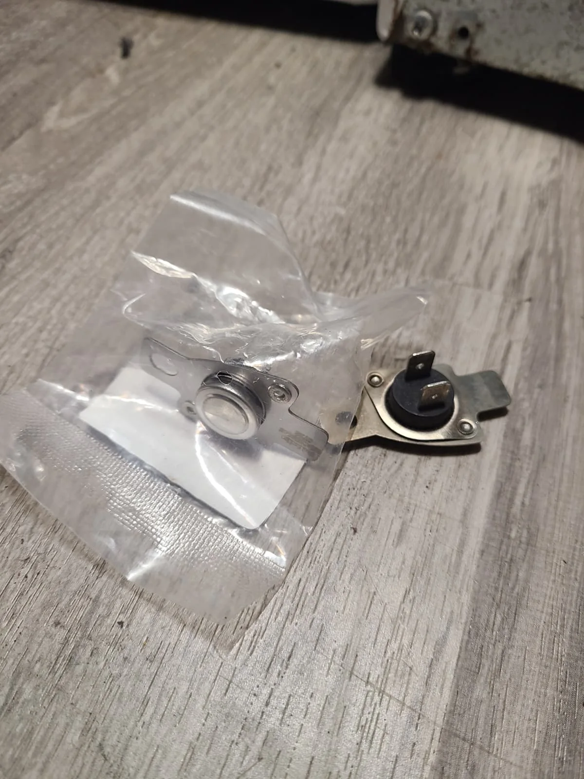 Removed dryer thermostat beside the replacement component in its packaging