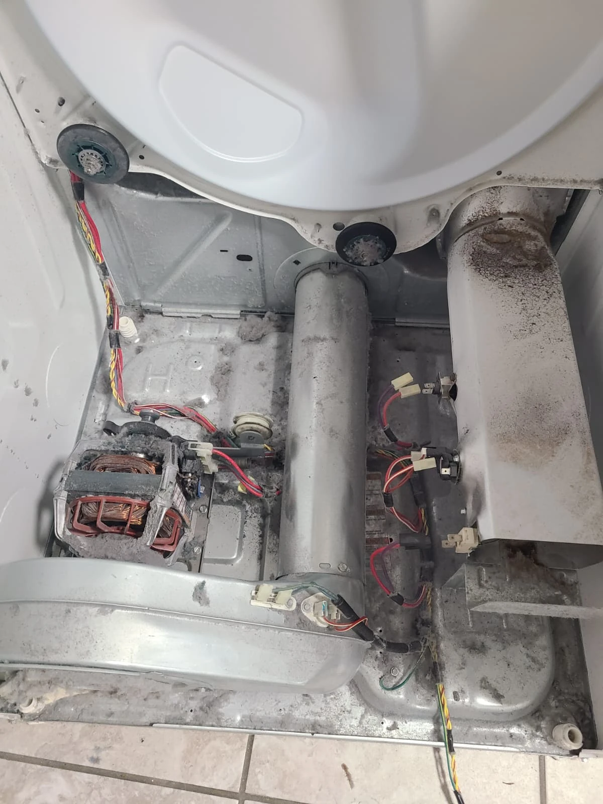 Dryer cabinet with drum removed, showing lint before interior cleaning