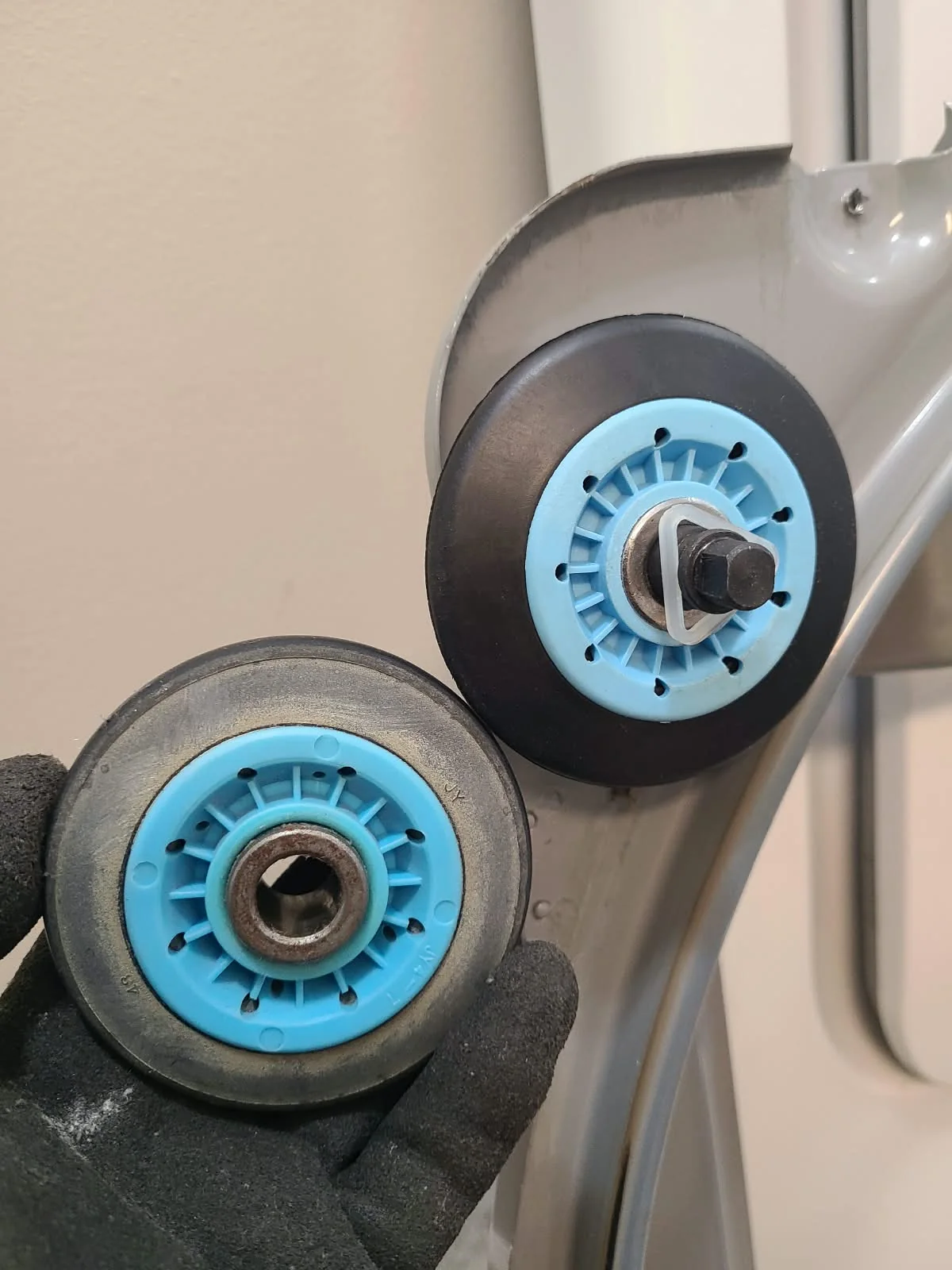 Removed drum support roller held beside a replacement roller installed on the support panel